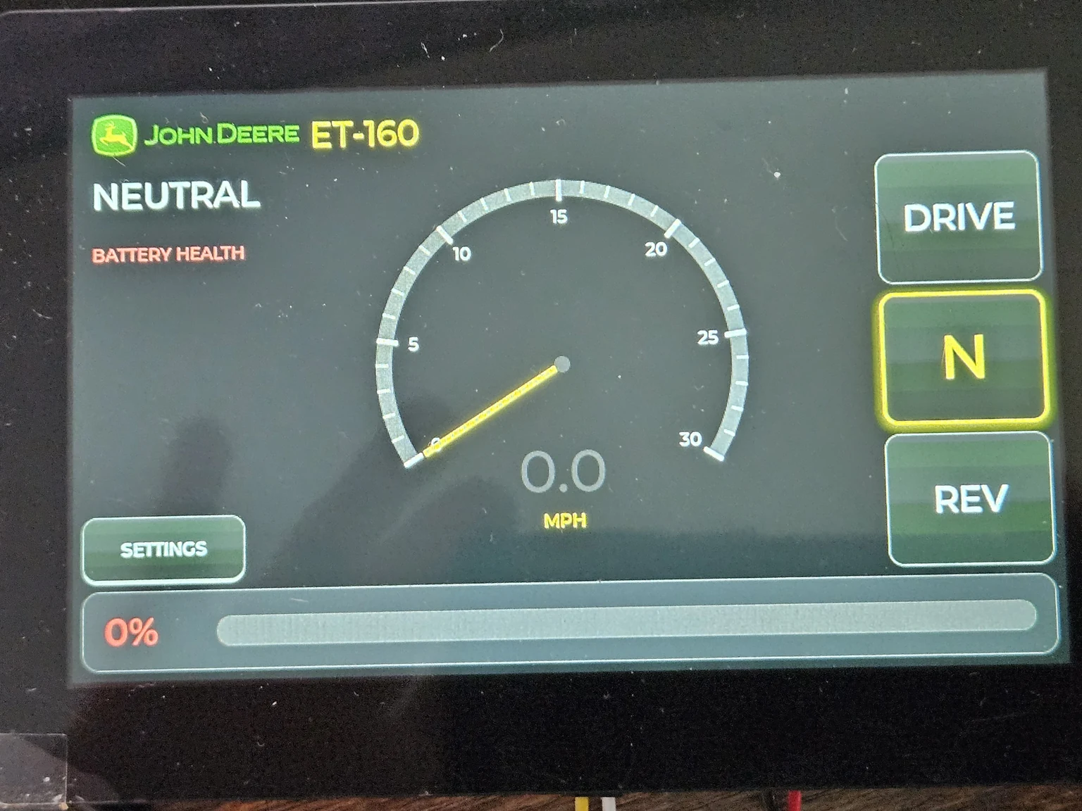 The ET-160 dashboard running on the real ESP32-S3 touchscreen: a John Deere ET-160 cockpit with a 0–30 MPH speedometer reading 0.0, NEUTRAL selected, DRIVE / N / REV gear buttons on the right with N highlighted green, a SETTINGS button, and a battery-health bar reading 0% because no pack is connected on the bench.